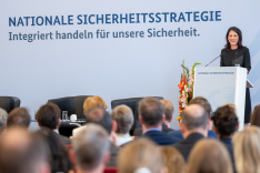 Außenministerin Annalena Baerbock steht an einem Redepult und spricht; den Hintergrund bildet eine Wand mit der Aufschrift "Nationale Sicherheitsstrategie"; im Vordergrund sitzen zahlreiche Menschen.