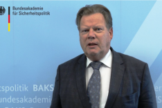 BAKS-Präsident a.D. Rudolf Adam steht vor einer blauen Pressewand der BAKS.