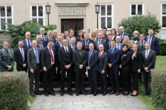 Eine Gruppe geschäftlich gekleideter Menschen, links im Bild ein militäruniformtragender Mann steht vor dem Haus Bonn der BAKS.