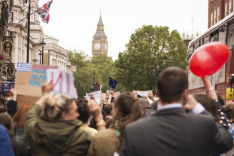 Peope walking on a street, in the background is a big tower with a clock and the union jack.