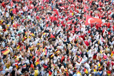 Das Bild zeigt eine beieinander stehende Menschenmenge, deren eine Hälfte als Fans der deutschen Fußball-Nationalmannschaft, die andere als Fans der türkischen Fußball-Nationalmannschaft erkennbar ist.